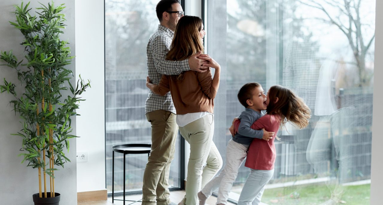 Happy parents and their small kids spending time together by the window at home. Copy space. Focus is on parents.